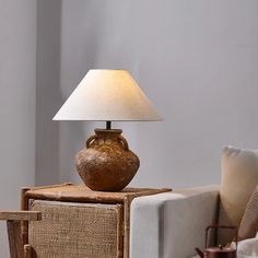 a brown vase sitting on top of a wooden table next to a white pillow and lamp