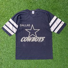 - 🏈 Vintage 1993 NFL Dallas Cowboys V Neck T-Shirt - 🎨 Navy blue tee in a large size - 🖼️ Features a prominent big graphic - ⭐ Authentic retro design from '93 - 🌟 Classic Cowboys team representation - 🏟️ Perfect for NFL enthusiasts - 🎉 Adds nostalgic sports vibe to your outfit - 💫 Comfortable and stylish wear - 🌈 Navy hue with bold graphic detail - 👕 Ideal for casual or game-day attire 📏Measurement:📏 Size on Tag: L Width (Pit to Pit): 21" Length (Neck to end of garment): 29" Sleeve Length (Neck to end of cuff): 18" 👕Condition: Good condition. Got yellow stain on sleeve. Please refer photos 🚚Shipping: Using Fedex Express shipping. 3-7 days delivery time 🚛Return: Please refer our policy E64-US4 College Throwback T-shirt With Team Logo, 90s Style Short Sleeve T-shirt For Game Day, Throwback Letter Print T-shirt For College, Vintage Cotton Tops With Team Logo, Vintage Crew Neck Top With Team Logo, 90s Style Screen Print T-shirt For Sports Events, Throwback College T-shirt With Screen Print, Throwback Graphic T-shirt For College, Vintage Graphic Print T-shirt For Sports Events