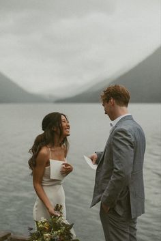 a man and woman standing next to each other in front of a body of water