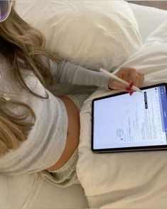 a woman laying in bed while holding an electronic device with a notepad on it