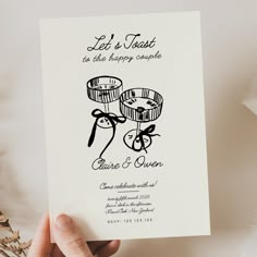 a hand holding up a wedding card that says let's toast to the happy couple