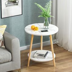 a white table with two oranges on it in front of a gray couch and window