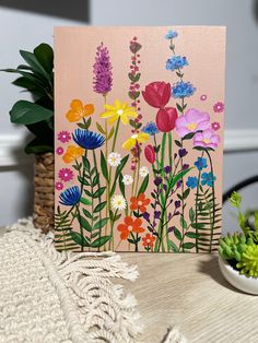 a card with flowers painted on it next to a potted plant