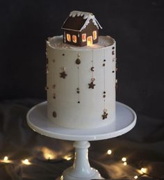 a white cake topped with a small house on top of a table covered in lights