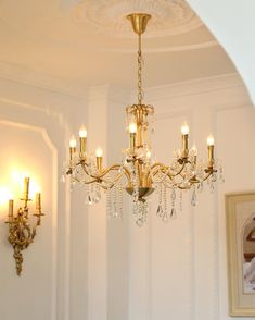 a chandelier hanging from the ceiling in a room with white walls and gold trim