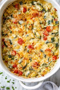 a casserole dish filled with cheese, tomatoes and spinach on a marble surface