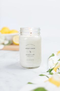 a white candle sitting on top of a table next to some lemons and flowers