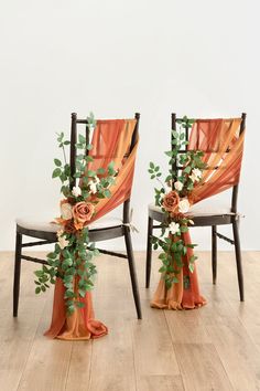 two chairs decorated with flowers and greenery on wooden floor next to each other in front of white wall