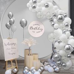 a birthday party with silver and white balloons on the wall, signs and decorations in front of it