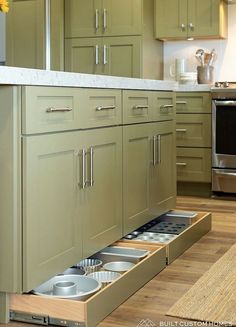 an open drawer in the middle of a kitchen with stainless steel appliances and green cabinets