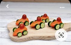 carrots and cucumbers are arranged in the shape of cars on a cutting board