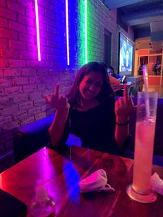 a woman sitting at a table with a drink in front of her and the lights on behind her