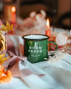 a green coffee mug sitting on top of a table next to flowers and candles in the background