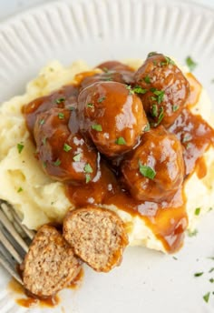 a white plate topped with mashed potatoes covered in meatballs and gravy