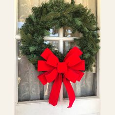 a christmas wreath on a window sill with a red bow