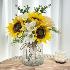 a vase filled with sunflowers and daisies on a table next to a candle