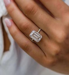 a close up of a person wearing a ring with an emerald cut diamond on it