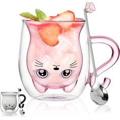 a glass mug with a cat face and strawberries in it, next to a spoon