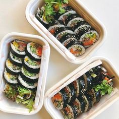 three plastic containers filled with sushi on top of a white table next to each other