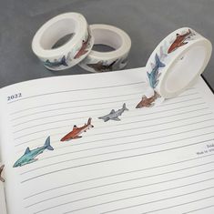 two rolls of washi tape sitting on top of an open notebook with shark drawings