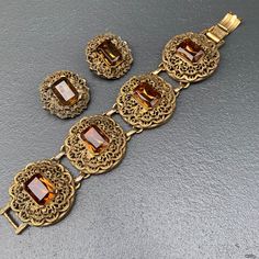 WIDE ~ massive / heavy ~ Vintage ~ Victorian revival ~ gold tone filigree ~ panel bracelet with faceted amber glass cabs ~ Bracelet comes with matching clip-on earrings Unsigned beauty ... Dates mid 20th century Material : gold tone metal amber color glass cabs Measurements : Bracelet is 7 3/4 inches x 1 1/2 inches wide . Earrings are 1 1/4 inches in diameter Condition : Overall all pieces are in good vintage condition with some age related wear ~ can see metal discoloration /darkening ~ Some li Ornate Gold Bracelets With Jewels, Antique Jeweled Metal Jewelry, Jeweled Antique Gold Brass Jewelry, Victorian Style Jeweled Gold Jewelry, Victorian Jeweled Gold Jewelry, Formal Antique Gold Jewelry With Antique Finish, Formal Antique Gold Jewelry, Vintage Antique Gold Jeweled Jewelry, Vintage Bronze Jeweled Jewelry