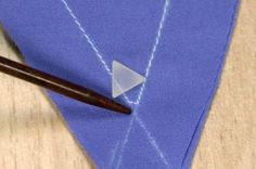 a piece of fabric with a triangle on it and a needle in the middle next to it