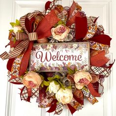 a welcome wreath with flowers and ribbons on the front door to someone's home