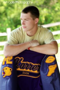 a young man sitting on the ground with his arms crossed, holding onto a jacket