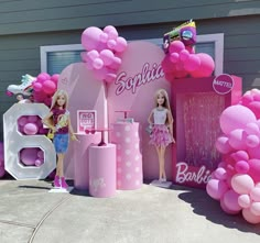 two barbie dolls are standing in front of a pink balloon - filled display with balloons