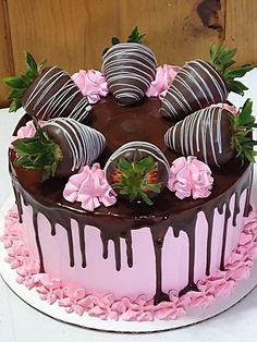 a chocolate covered cake with pink flowers and strawberries on the top is sitting on a table