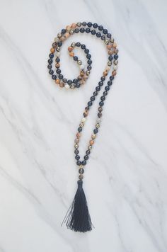 the multicolored beaded necklace with black tassels and gold beads is on a marble surface