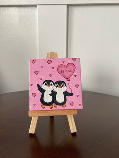 a small easel with two penguins on it and a heart balloon in the background