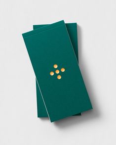 two green envelopes with gold buttons on the front and back, sitting next to each other