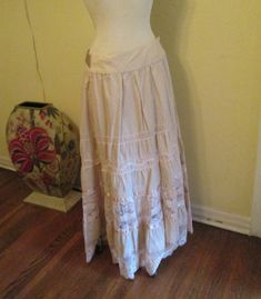 Vintage Bebe maxi skirt lace trim oatmeal color and gorgeous. This skirt is elegant with a boho style.  The waist is very flattering. It has inner buttons to wrap the skirt around. The skirt has wonderful embroidery with silk (or satin)ribbons and lace. You can tie the silk sash in the front, back or wrap around. It's made of a sturdy cotton and would look great with sandals or boots, can be worn with a tee shirt, a delicate blouse or short jacket (or any other way you think). Works for casual and dressy occasions. This skirt is suitable to be worn summer or winter. In excellent condition. It is marked small but please see measurements below, it could fit a medium poss a large. You also can move the buttons to tighten or loosen it. Measurements: Waist. 30" Hips. 42" full Length. 41" Thanks Beige Lace Long Skirt, Beige Flowy Lace Skirt, Beige Lace Tiered Skirt, Beige Lace Trim Skirt For Spring, Beige Skirt With Lace Trim For Spring, Beige Cotton Skirt With Lace Trim, Fitted Bohemian Lace Maxi Skirt, Summer Beige Lace Maxi Skirt, Beige Bottoms With Lace Trim Flowy Design