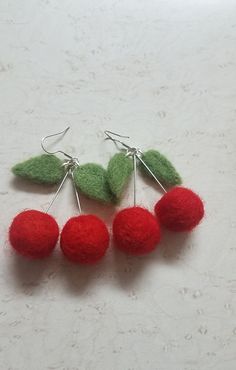 four cherries with green leaves and red balls on white table top, ready to be made into earrings or pendants