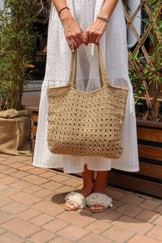 a woman in white dress holding a straw bag on brick ground next to planters