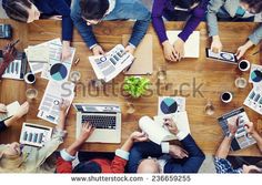 several people sitting at a table with laptops and papers on top of each other