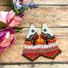 a pair of beaded earrings sitting on top of a wooden table next to flowers