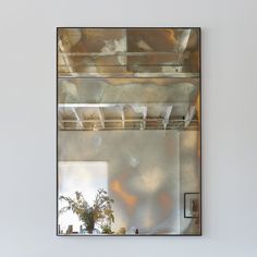 a mirror hanging on the wall above a table with a vase and potted plant