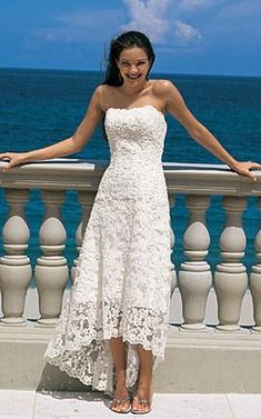 a woman in a white dress standing on a balcony next to the ocean with her arms outstretched