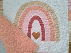 a quilted wall hanging with a rainbow and heart on the front, in pastel colors