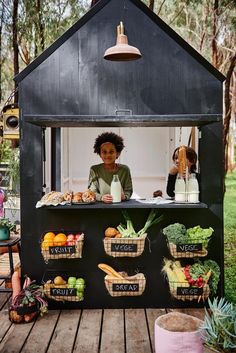 a woman standing behind a counter filled with fruits and vegetables