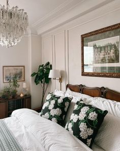 a bed with white sheets and pillows in a bedroom next to a chandelier