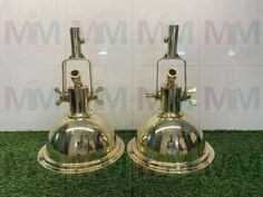 two shiny metal bell shaped lamps sitting on top of green carpeted floor next to a white wall