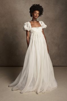 a woman in a white dress standing on a gray background with an afro hairstyle