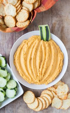 a bowl filled with hummus next to crackers and cucumbers on a table