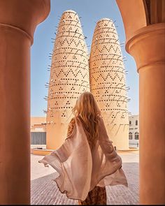 a woman is walking through an archway in front of two large white structures with spikes on them