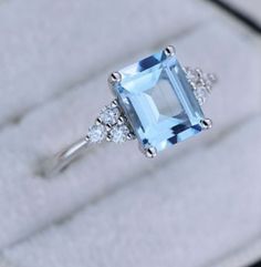 a ring with an aqua blue topazte surrounded by white diamonds in a box