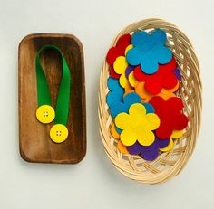 a basket filled with felt flowers next to a small wooden tray holding a green ribbon