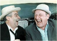 two men laughing while sitting next to each other in front of an old fashioned car